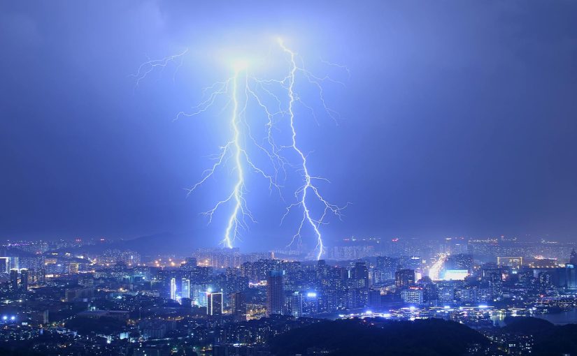 Breathtaking thunderstorm with lightning bolts over modern illuminated city at night with purple sky