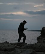 A man standing on rocks looking at his phone
