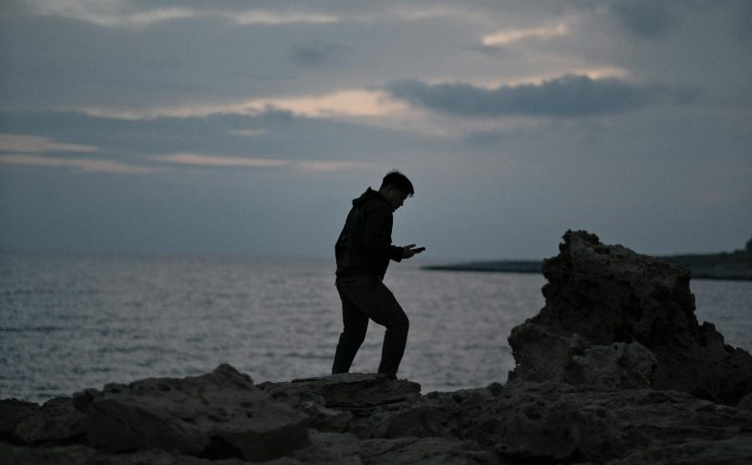 A man standing on rocks looking at his phone
