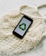 Overhead of smartphone with simple recycling sign on screen placed on white eco friendly mesh bag on marble table in room