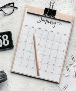 Top view composition of clipboard with calendar and pencil placed on desk amidst stationery and eyeglasses