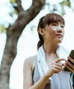 Contemplative Asian woman in bracelet browsing internet on smartphone in park