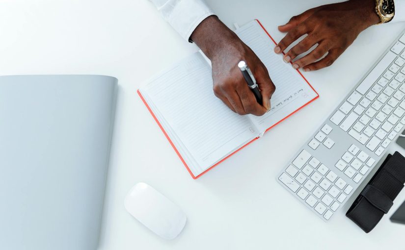 Person Writing on White Paper Beside Apple Magic Mouse